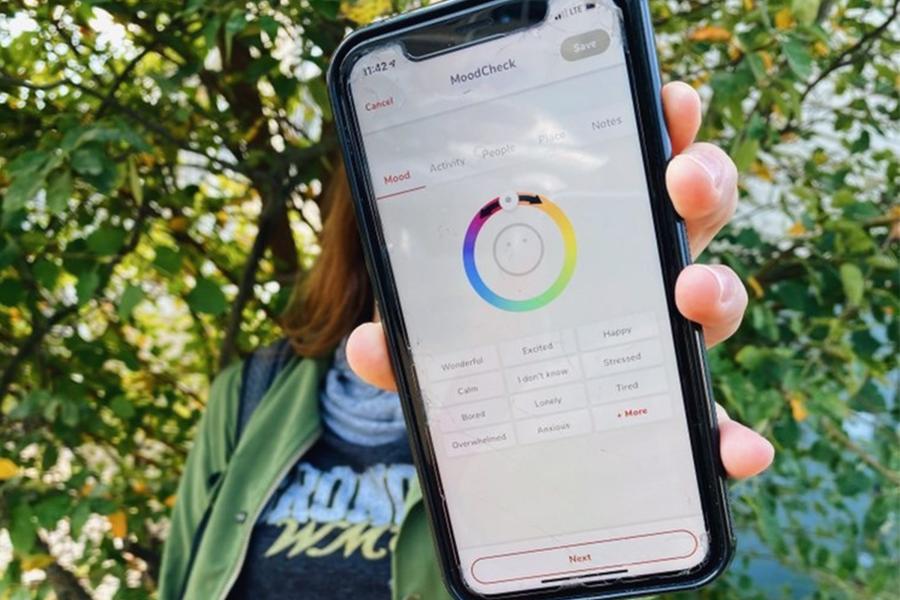 A student holding up a smartphone with the WellTrack app open.